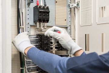 備屈をした手で電気パネルに配線する作業員